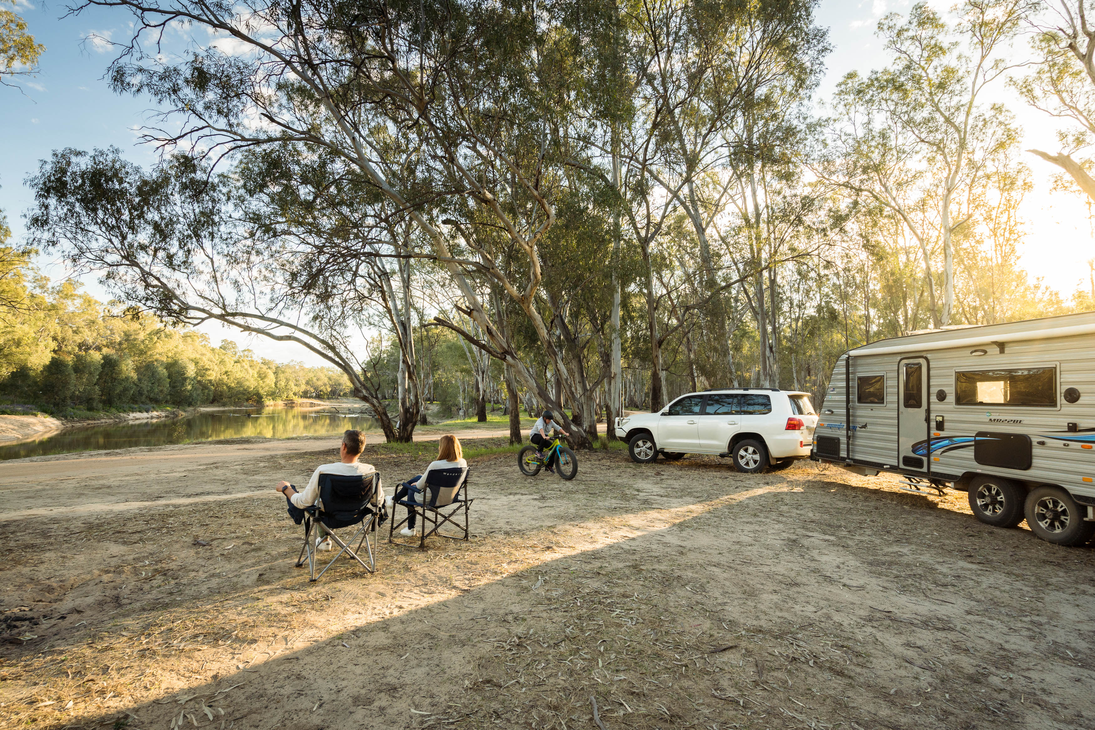 Couple in camping chairs with caravan and car, overlooking the Murrumbidgee River